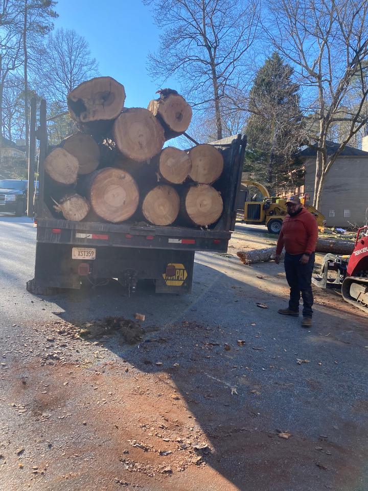 Log truck stacked with fresh trunk rounds on a residential street, a crew member standing beside it